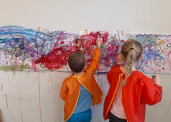 Zwei Kinder malen an eine Wand.